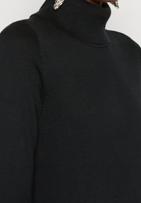 Maglione a collo alto nero realizzato in morbido tessuto a maglia, caratterizzato da una texture a coste e cuciture a vista sulle spalle.
