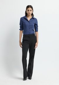 Blauw gestreept overhemd met opgerolde mouwen, gecombineerd met zwarte op maat gemaakte broek en scherpe zwarte schoenen. Eenvoudig, verfijnd ontwerp.