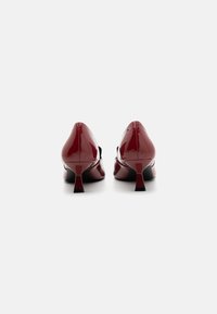 Red patent leather high heels with a pointed toe and a small, flared heel. The shoes feature a smooth, shiny surface and a sleek design.