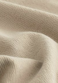 Tăiat dintr-un material textil bej, cu pliuri moi, având un model țesut subtil și o finisare netedă, delicată.