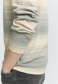 Zebrażowy sweter w paski, stworzony z połączenia jasnej kremowej i miękkiej szarości. Teksturowana tkanina z prążkowanymi mankietami i luźnym krojem.