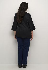 Camiseta negra de corte holgado con mangas de tres cuartos, combinada con jeans rectos azules y zapatos de plataforma negros. Textura de tela suave.