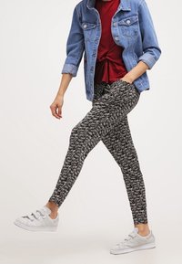 Legginsit mustavalkeassa abstraktissa kuosissa, yhdistettynä punaiseen paitaan ja farkkutakkiin. Päälle puettuna valkoiset lenkkarit, korostaen istuvaa muotoilua.