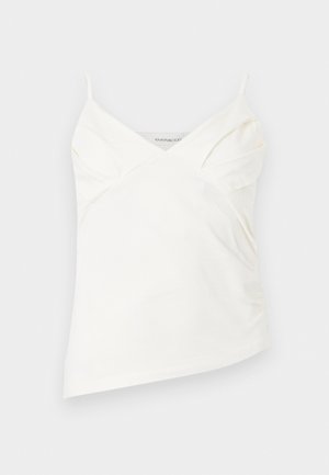 Ασύμμετρο λευκό τοπ μπλούζα με λεπτές τιράντες και διακριτικές ραφές στο μπούστο, απεικονιζόμενο σε απλό φόντο.