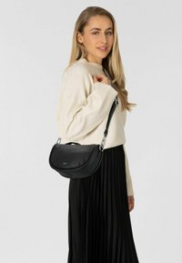 Zwarte leren handtas met een gebogen vorm, zilveren hardware en een bovenhandgreep. Draag de tas over de schouder tegen een lichte achtergrond.