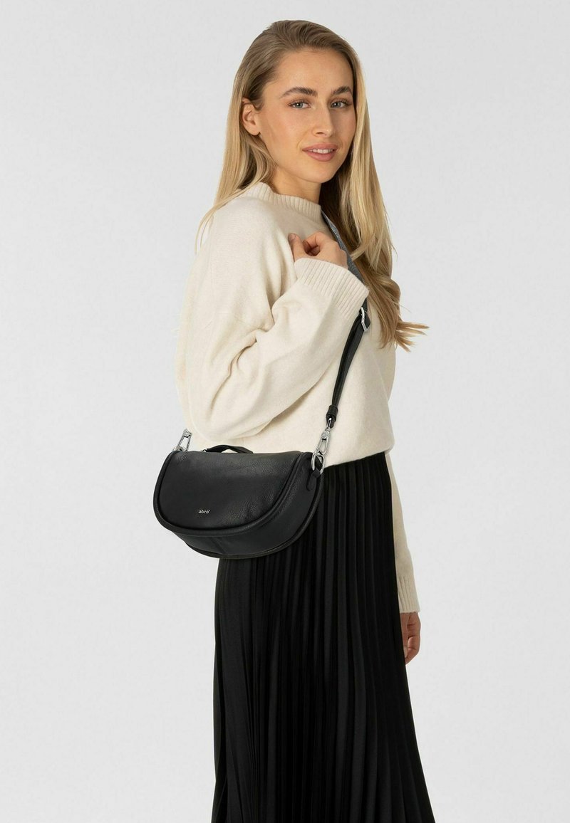 Zwarte leren handtas met een gebogen vorm, zilveren hardware en een bovenhandgreep. Draag de tas over de schouder tegen een lichte achtergrond.