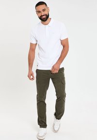 Hvid polo tee med korte ærmer, knapkrave; olivengrøn cargo-bukser med sidelommer; beige og hvide sneakers.