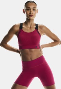 Fuchsia sports bra with black adjustable straps and a smooth, textured finish. Paired with matching fuchsia high-waisted shorts.