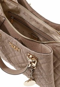 Borsa trapuntata beige con dettagli in metallo dorato, chiusura con cerniera e tasche interne, logo in rilievo e ciondolo decorativo removibile.