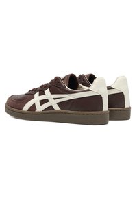 Paire de baskets basses marron avec des bandes blanches et des accents au talon, semelle texturée et fermeture à lacets, vues de l'arrière côté.