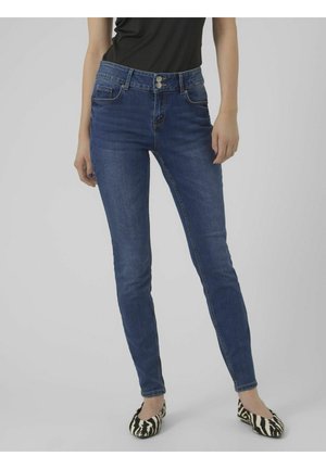 Skinny blue jeans made from denim, featuring a high waist, five pockets, and two-button closure. Worn with black top and patterned flats.