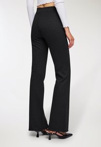 Czarne spodnie w prążki z szerokimi nogawkami, wykonane z gładkiego materiału. Dopasowany stan z klasycznym krojem, zestawione z czółenkami z ostrym noskiem.
