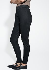 Leggings neri elasticizzati realizzati in tessuto morbido, con vita alta e vestibilità aderente, abbinati a scarpe nere e a un top marrone texturizzato.