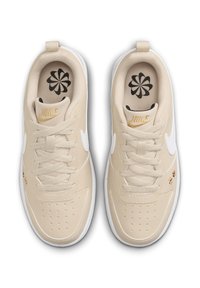 Bež Nike športni copati z belimi detajli, strukturiran sintetični zgornji del, ravne vezalke in podplat s patterned notranjostjo, ki ima cvetlični vzorec.