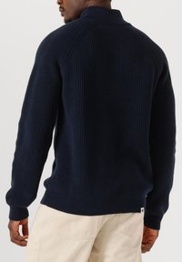 Maglione a coste di colore blu navy con colletto alto, maniche lunghe e orlo aderente. Presenta un piccolo logo in basso a sinistra.