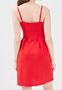 Rød kjole med tætsiddende bodice, tynde stropper og plisseret nederdel. Stoffet ser glat og let ud og slutter over knæet.