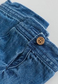 Shorts in denim di blu medio con una finitura testurizzata, caratterizzati da un bottone rotondo in legno, una cintura cucita e tasche laterali.