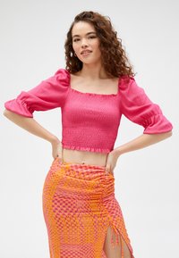 Lyserød cropped bluse med smocked tekstur og puffærmer, parret med en livlig mønstret nederdel med cirkler i lyserøde og orange nuancer.