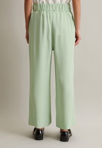 Hellgrüne, weit geschnittene Hose mit elastischem Bund und glatter Textur, ausgestattet mit einem schlichten Saum ohne zusätzliche Details.