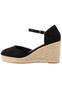 Schwarzer Wildleder-Wedge-Schuh mit runder Zehenform, Knöchelriemen und gewebtem Jute-Wedge-Absatz. Glatte Textur mit geflochtenem Detail am Absatz.