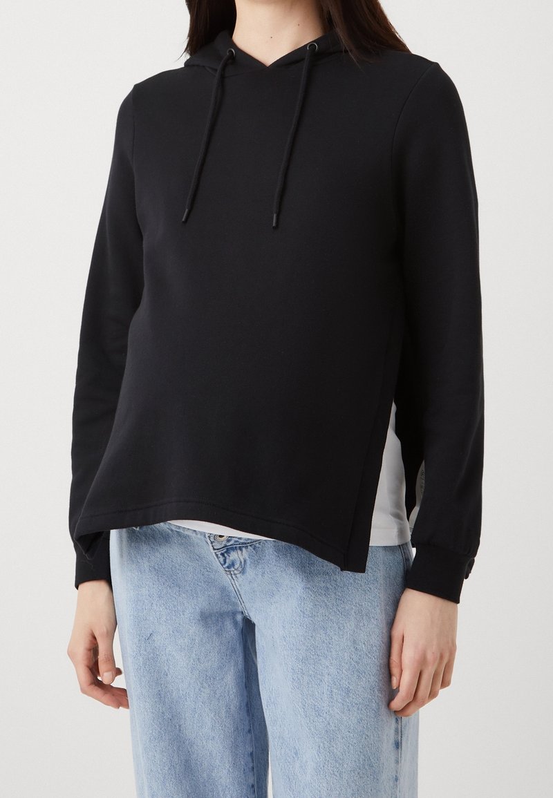 Black hooded sweatshirt with long sleeves, drawstring detail, and a relaxed fit, paired with light blue denim jeans.