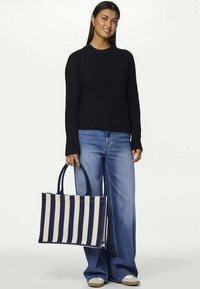 Saco de lona com riscas verticais em azul marinho e creme, apresentando duas alças resistentes, combinado com um suéter preto e jeans de perna larga azul.