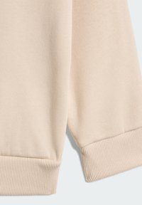 Beżowy sweter o fakturowanym materiale, z prążkowanymi mankietami i luźnym krojem. Tkanina wydaje się miękka i ma lekką jakość.