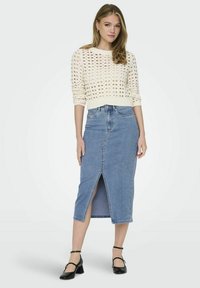 Krämfärgad stickad tröja med ett öppet mönster, åtföljd av en ljusblå denimpennkjol med en framficka. Svarta klackskor fulländar looken.