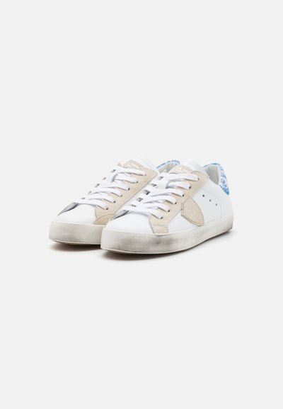 Hvite sneakers med beige semsket detaljer, flat gummisåle, tekstilheeldetaljer og hvite lisser. Litt slitt utseende på sålen.