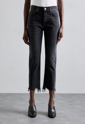 Jeans in denim nero con un design a gamba dritta e cropped, orlo sfrangiato e tasche frontali, abbinati a mule nere.