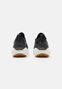 Black athletic shoes with a textured mesh upper, rubber heel, and a white sole with a gum outsole. Features a logo on the heel.