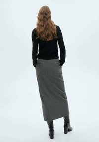 Langer grauer Pinstriped-Rock aus weichem Stoff, kombiniert mit einem schwarzen, enganliegenden Pullover. Die Person trägt knielange schwarze Lederstiefel.