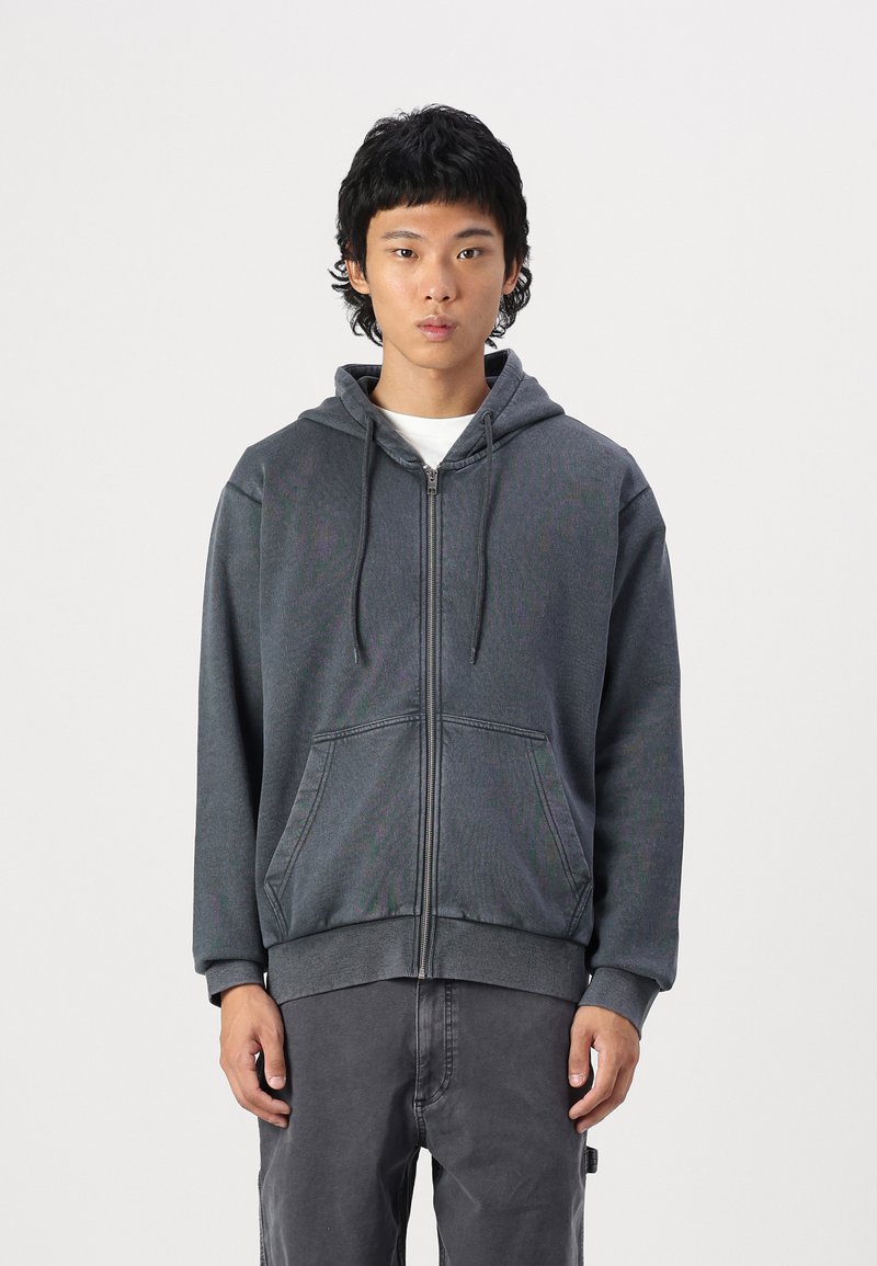 Gray zip-up hoodie with a drawstring hood, front pockets, and ribbed cuffs. The fabric has a smooth texture and a relaxed fit.