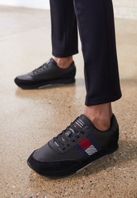 Sneakers neri con accenti in suede testurizzato, caratterizzati da un design a strisce rosso, bianco e blu sui lati. Suola in gomma, chiusura con lacci.