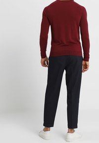 Vinröd stickad tröja med långa ärmar, figursydd design och rundad halsringning, kombinerad med marinblå byxor och vita sneakers.