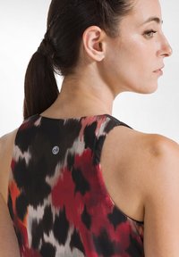 Mouwloos, meerkleurig top met een abstract patroon in rood, zwart en grijs. Soepele textuur met een klein logo op de achterkant van de halslijn.
