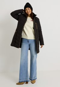 Doudoune noire avec texture matelassée et accents dorés, associée à un pull crème et un jean évasé bleu clair. Complété par un bonnet en tricot noir.