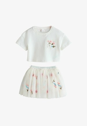 Fehér pamut rövid felső virágos hímzett zsebbel; fehér réteges tüll szoknya színes virágmintákkal és rugalmas derékpánttal.