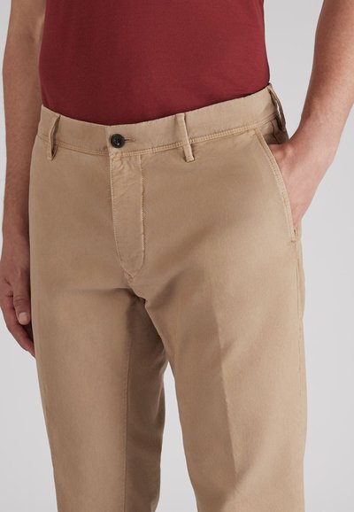 Beżowe bawełniane spodnie o prostym kroju, z czarnym guzikiem w pasie, bocznymi kieszeniami i gładką fakturą.