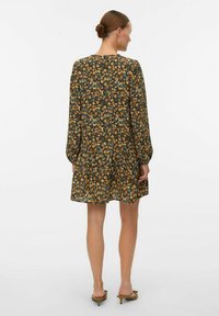 Robe fleurie en vert foncé avec une jupe froncée, des manches longues et un col rond. Agrémentée de fleurs orange et jaunes.
