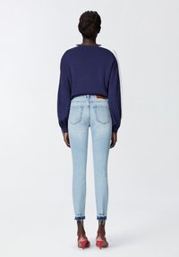 Maglione blu navy con dettagli bianchi, abbinato a jeans skinny azzurri chiari. I jeans presentano un orlo sfilacciato e un'etichetta in pelle beige sulla vita posteriore.