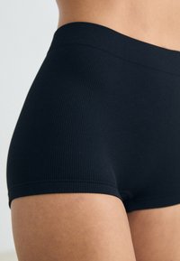 Schwarze gerippte Hipster-Shorts aus Stoff mit einem glatten Bund, die eine enganliegende Passform und ein nahtloses Design für hohen Komfort bietet.