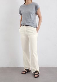 Jasnoszara koszulka z podwiniętymi rękawami, kremowe spodnie z szerokimi nogawkami, czarny pasek oraz płaskie sandały z detalem w złotym kolorze. Gładka faktura materiału.