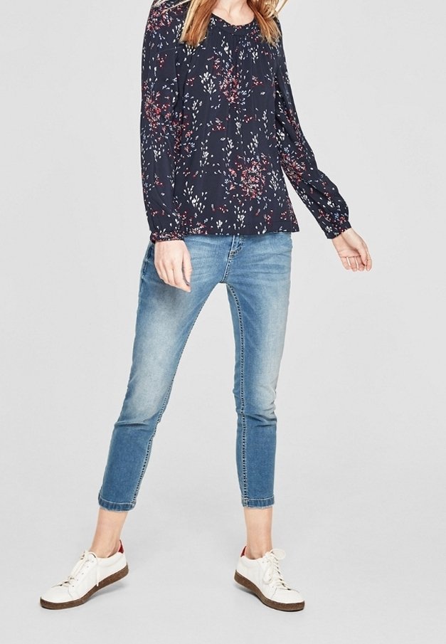 Blusa a maniche lunghe floreale blu navy con polsini aderenti, abbinata a jeans azzurri alla caviglia e sneakers bianche con suola marrone.