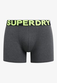 Boxers ajustados de color gris, con una cinturilla negra impresa con "SUPERDRY" en una fuente verde brillante. Textura suave y sin patrones.