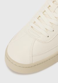 Crème-kleurige leren sneaker met een gladde textuur, ronde neus en platte veters, met een contrasterende beige rubberen zool.