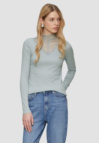 Lichtblauw langemouwen top met een hoge kanten kraag en geometrisch patroon, gecombineerd met lichtblauwe denim jeans. Gladde textuur, aansluitend ontwerp.