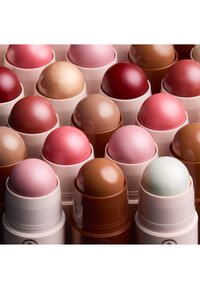 Rangées de cosmétiques sous forme de bâtonnets arrondis dans diverses nuances de rose, marron, rouge et beige avec des finitions brillantes et mates.