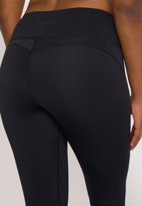 Zwarte high-waisted legging gemaakt van gladde, rekbare stof. Bevat flatlock naden en subtiele logo-details op de tailleband.