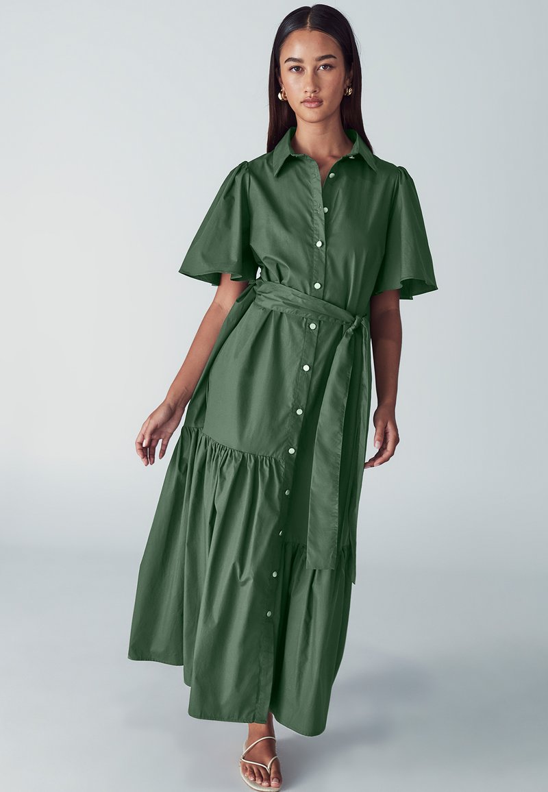 Zelené maxi šaty z bavlny s krátkými volánovými rukávy, předními knoflíky, vázacím páskem v pase a vrstvenou sukní. Hladká textura a neformální design.